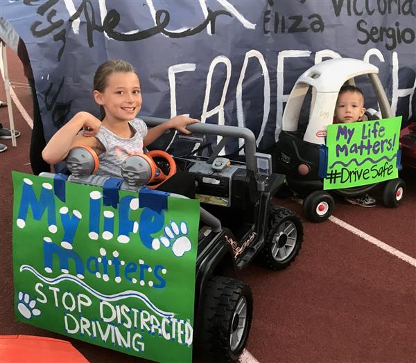 Two small children sit in toy cars with distracted driving slogans posted on the cars. Two small children sit in toy cars with distracted driving slogans posted on the cars.
